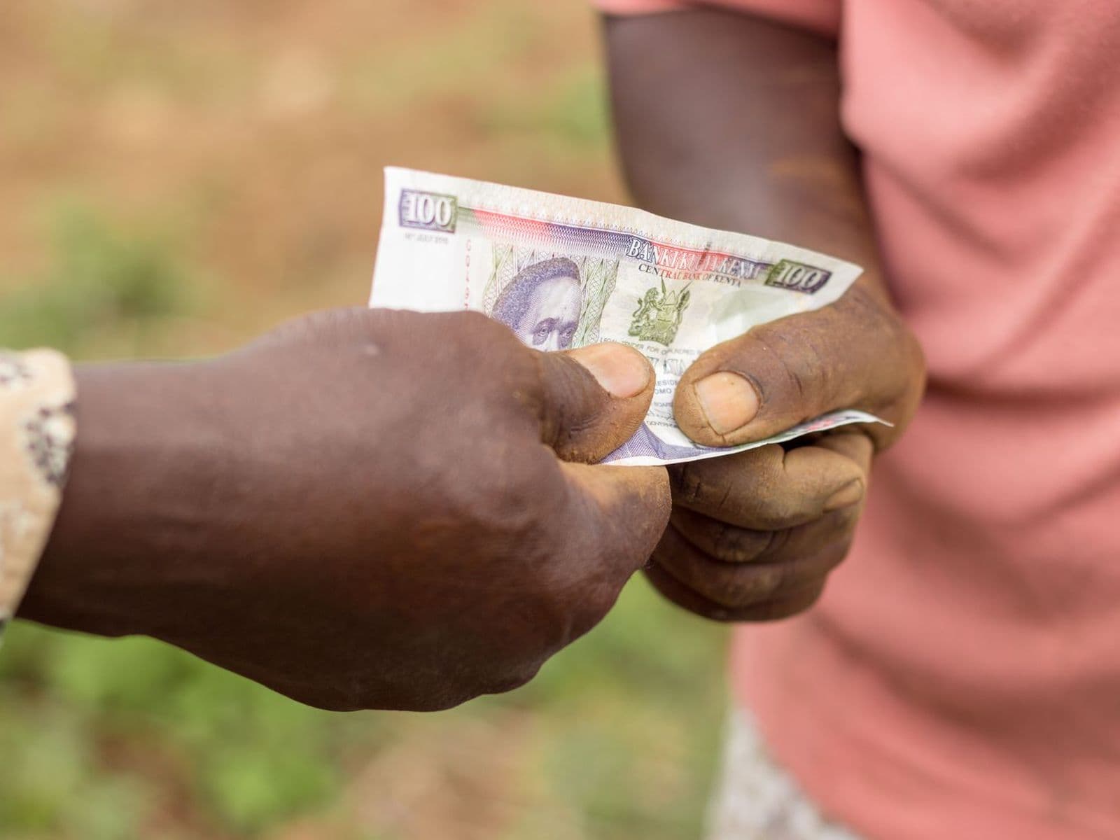 A hand passing a Kenyan hundred-shilling note to another
