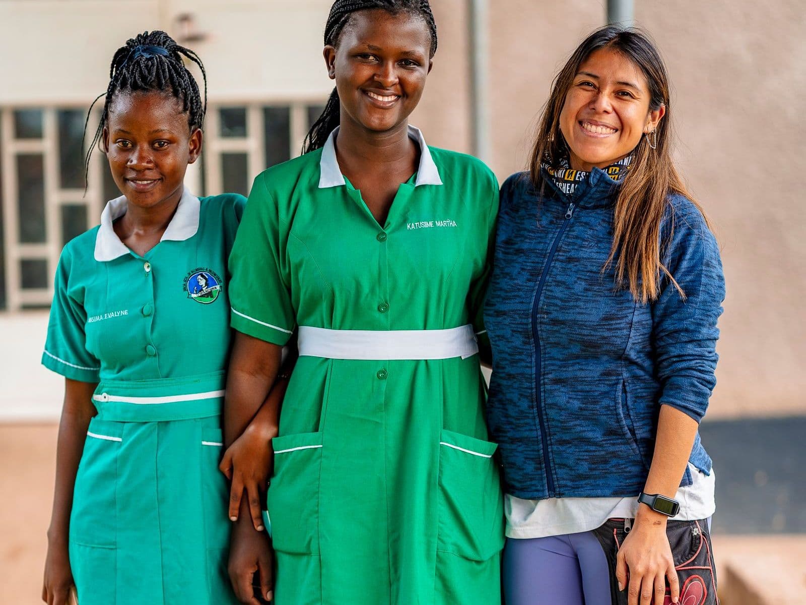 Two nurses in uniform and a colleague, smiling outside a hospital
