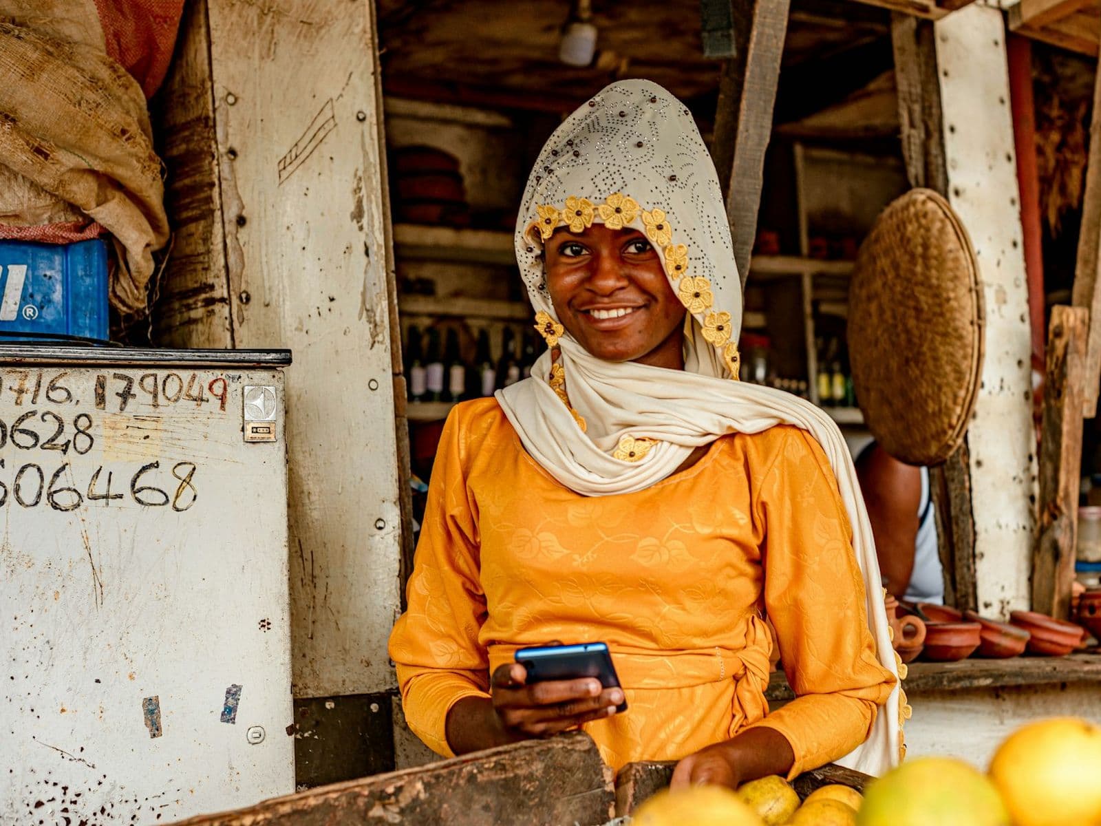 A fruit seller at her stall, smiling at her phone